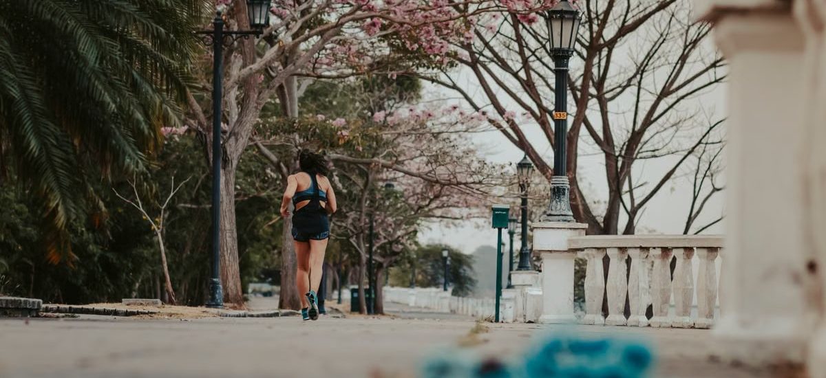A woman jogs through a picturesque park lined with blooming spring trees and vintage lamps.
