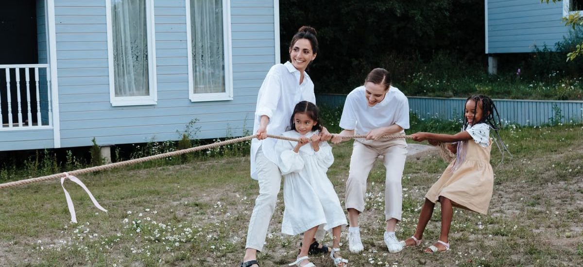A happy family enjoys a game of tug of war in a grassy field by a house.